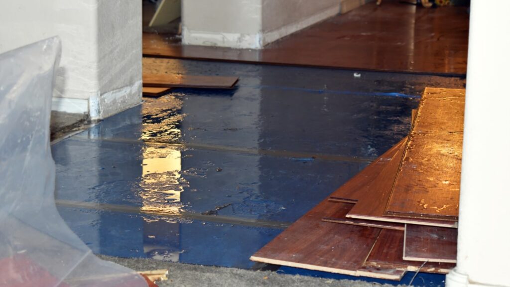 Wooden boards from a floor are removed revealing pools of water on the ground.