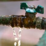 An old and grimy pipe leaking clear water.
