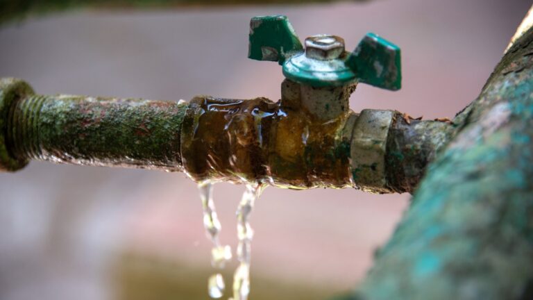 An old and grimy pipe leaking clear water.