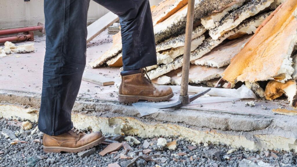 A man in boots stands next to a pickaxe on a home restoration site.