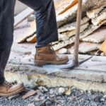 A man in boots stands next to a pickaxe on a home restoration site.