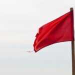 A cloudy sky with a red flag waving on a wooden pole.