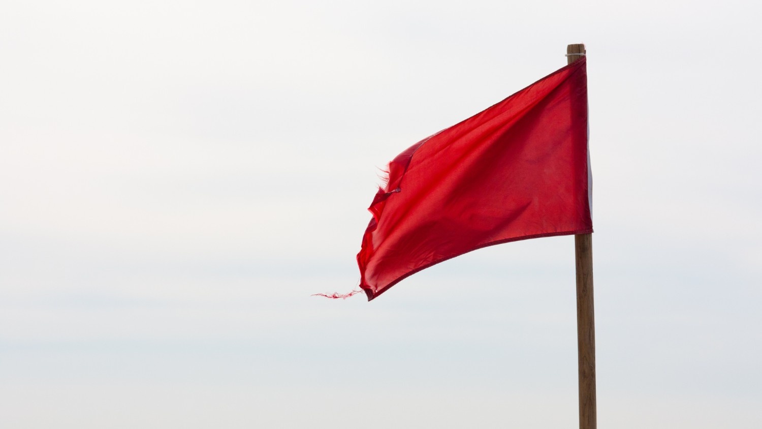 A cloudy sky with a red flag waving on a wooden pole.