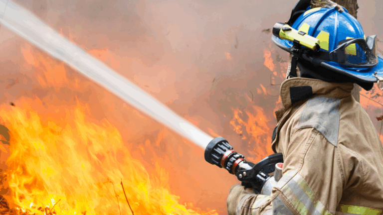 A firefighter wearing a blue helmet uses a fire hose to fight a large flame.